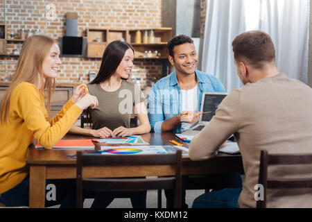 Quattro allegro colleghi seduti insieme e discutere il loro progetto straordinario Foto Stock