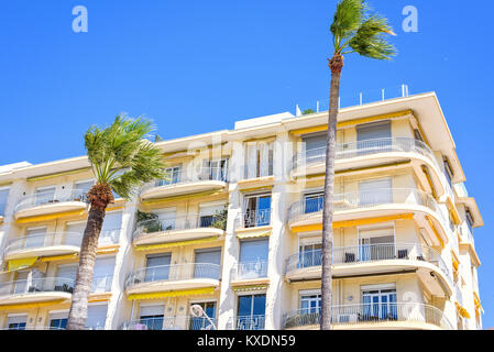 La luce diurna luminosa vista al giallo hotel balconi su palme sfondo. Azzurro cielo chiaro. Copia negativo di spazio e posto per il testo. Auto parcheggiate su Foto Stock