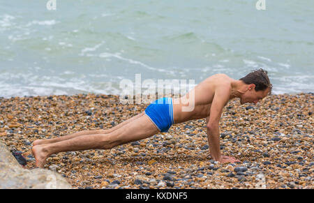 Uomo che indossa solo shorts facendo esercizi del mattino (pushups, push ups, pressups, premere ups) su una spiaggia in un freddo giorno nel Regno Unito. Foto Stock