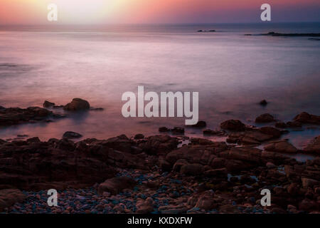 Tramonto sull'oceano su uno sperone roccioso costiero. Prese a Sennen Cove in Cornovaglia Regno Unito che guarda all'Oceano Atlantico. Foto Stock