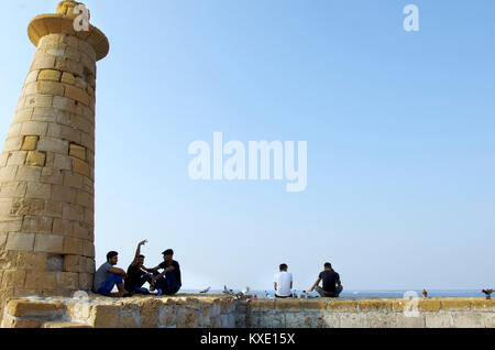 La gente del posto reaxing insieme su una parete accanto a un faro nella zona del porto di Kyrenia, Cipro Foto Stock