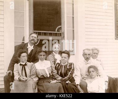 Antique circa 1905 fotografia, famiglia riunita su stoop dalla porta dello schermo. La posizione è in o vicino a Riggsville (ora Robinhood), Maine in Sagadahoc County, Stati Uniti d'America. Foto Stock