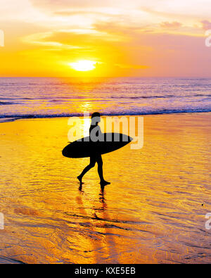 Donna surfer di camminare sulla spiaggia con la tavola da surf al tramonto. Isola di Bali