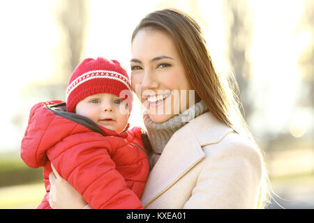 Ritratto di una madre felice in posa con il suo bambino figlio guardando a voi all'aperto in inverno Foto Stock