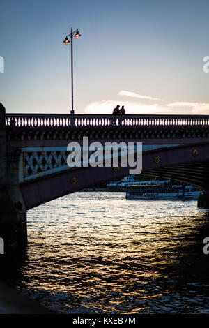 Due persone che si stagliano dal cielo della sera come stanno su Blackfriars Bridge sul fiume Tamigi a Londra Foto Stock
