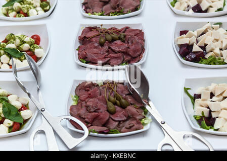 Piatto di Salumi con capperi. Affettati in una piastra bianca con capperi su un tavolo bianco. Carne con capperi Foto Stock