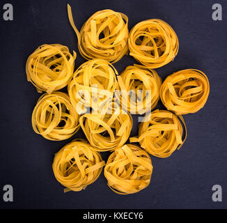 Grano cruda pasta in forma di nidi su uno sfondo nero, vista dall'alto Foto Stock