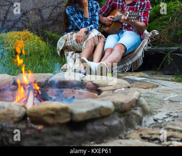 Coppia giovane con la chitarra vicino a fuoco all'aperto. Viaggi e vacanze concept Foto Stock