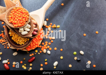 Varie materie i legumi in cucchiai di legno su sfondo nero Foto Stock