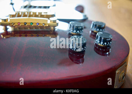 Tono e volume manopole su un lucido rosso vino Chitarra con Hardware dorato collocato su un tavolo di legno Foto Stock