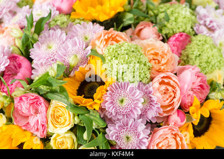 Bouquet di fiori misti in un vaso sul tavolo in legno. Il lavoro del fioraio presso un negozio di fiori. un brillante mix di girasoli, crisantemi e rose. sfondo sullo schermo intero Foto Stock