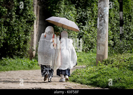 Due ortodossa etiope di donne che indossano mantelli bianchi voce verso la chiesa con ombrellone ad Addis Abeba in Etiopia Foto Stock