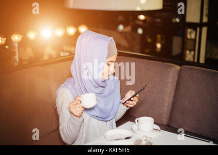 Donna musulmana messaggi su un telefono cellulare in cafe Foto Stock