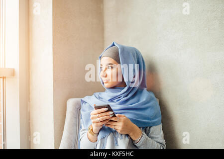 Donna musulmana messaggi su un telefono cellulare in cafe Foto Stock