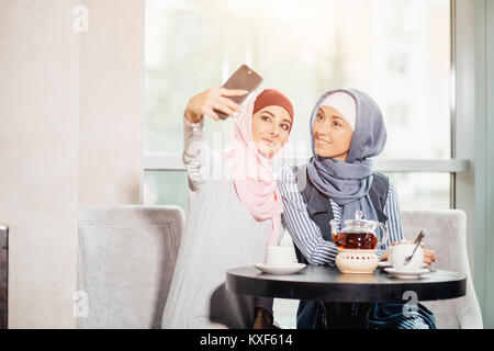Due felice giovane donna musulmana prendere autoritratto con handphone presso il cafe Foto Stock