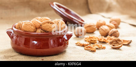 Le noci in un vaso di ceramica su una tela ruvida Foto Stock