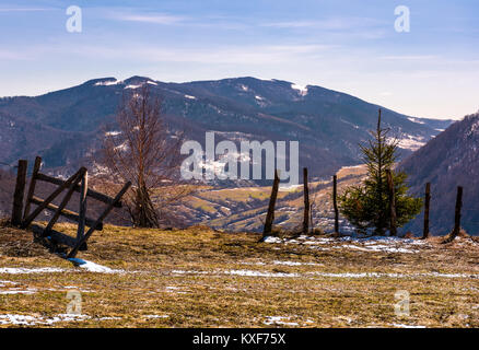 Rotture di recinzione di legno sulla collina. La primavera è in arrivo. bellissimo paesaggio di montagna con un po' di neve sulle piste con erba spiovente su un luminoso giorno Foto Stock