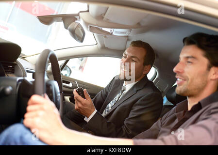 Venditori di auto e i clienti a parlare della tecnologia di un auto nello showroom di una concessionaria auto Foto Stock