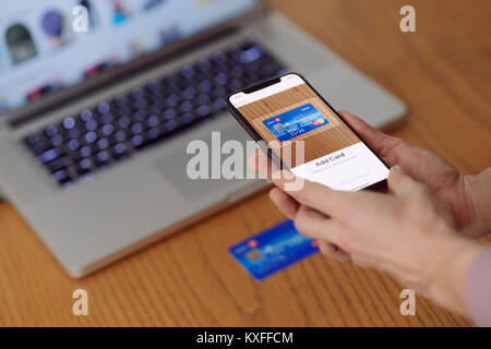 Donna con iPhone X nella sua mano la scansione di una carta di credito con Apple paga, Apple portafogli elettronici di pagamento app Foto Stock