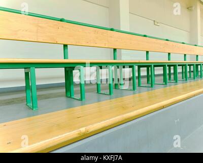 Righe vuote di panche di legno nella scuola sala sportiva. Tribune in palestra per gli appassionati di fiammiferi vuote con posti a sedere in legno. Foto Stock