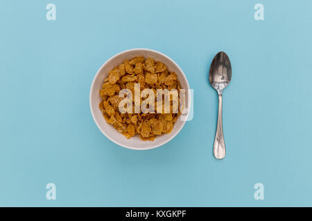 Cereali per la prima colazione cornflakes nella ciotola con cucchiaio d'argento su sfondo blu Foto Stock