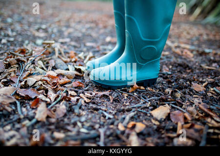 Un uomo o una donna che indossa un paio di tradizionali in gomma verde stivali da pioggia in un bosco in autunno con foglie e rametti sul terreno Foto Stock