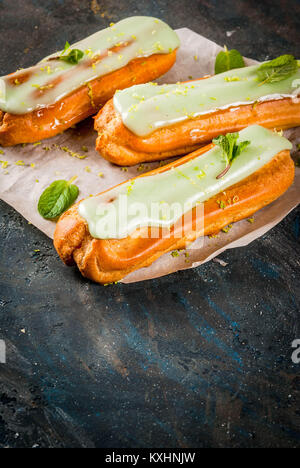 Tradizionale Francese dessert. Il Mojito Eclairs con la scorza del lime e foglie di menta, su sfondo blu scuro, spazio di copia Foto Stock