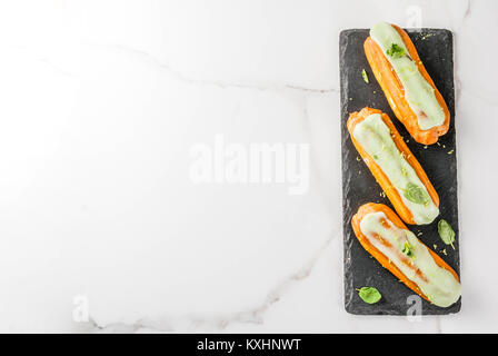 Tradizionale Francese dessert. Il Mojito Eclairs con la scorza del lime e foglie di menta, su sfondo blu scuro, spazio copia vista superiore Foto Stock