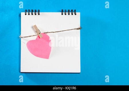 Notebook bianco su molle con un cuore di carta avvolto in una fune su uno sfondo blu Foto Stock
