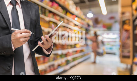 Imprenditore utilizzando il tablet e iscritto all'ordine magazzino il supermercato blur sullo sfondo, business concetto tecnologico Foto Stock