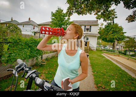 Femmina matura ciclista bere da una bottiglia d'acqua in giardino Foto Stock