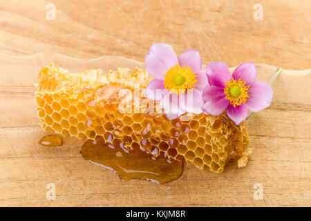 Il miele Il miele di gocciolamento pettine con fiori su tavola di legno Foto Stock