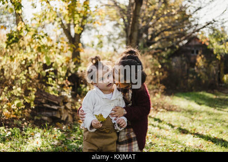 Ragazza abbracciando sorella più giovane, in ambiente rurale Foto Stock
