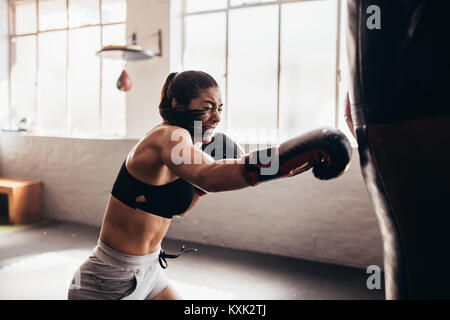 Boxer femmina di colpire un enorme sacco da boxe presso un studio di inscatolamento. Donna boxer allenamento duro. Foto Stock