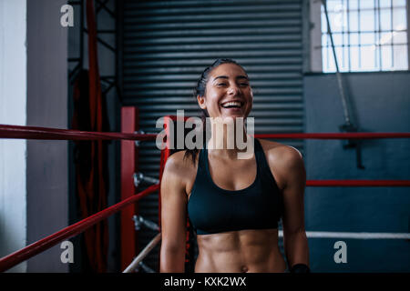 Sorridente boxer femmina seduto in un angolo di un pugilato ring durante la sua formazione. Boxer di formazione presso un studio di inscatolamento. Foto Stock