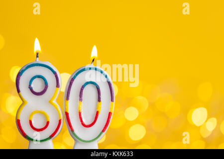 Numero 80 celebrazione di compleanno candela contro un luci luminose e sfondo giallo Foto Stock