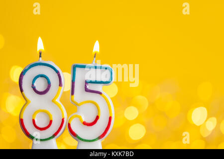 Numero 85 celebrazione di compleanno candela contro un luci luminose e sfondo giallo Foto Stock