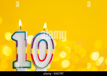 Numero 10 celebrazione di compleanno candela contro un luci luminose e sfondo giallo Foto Stock