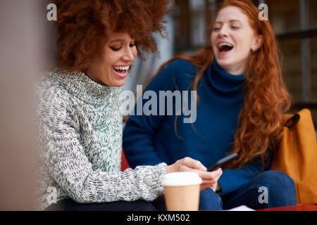 Gli amici presso la caffetteria utilizzando mobile telefono ridendo Foto Stock