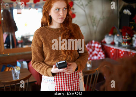 Cameriera in cafe tenendo il lettore di carte di credito Foto Stock