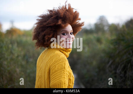 Ritratto di donna con afro guardando sopra la spalla alla fotocamera a sorridere Foto Stock