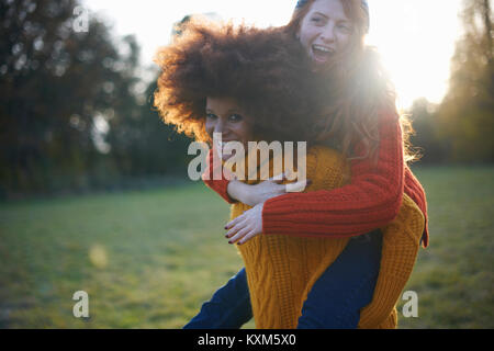 Due giovani donne,in ambiente rurale,giovane donna dando amico piggyback ride Foto Stock