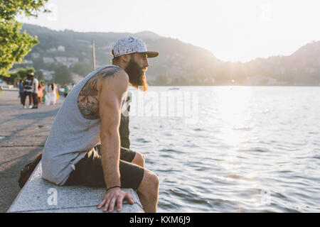 Giovane maschio hipster seduti sulla parete che guarda al lago di Como,Lombardia,Italia Foto Stock