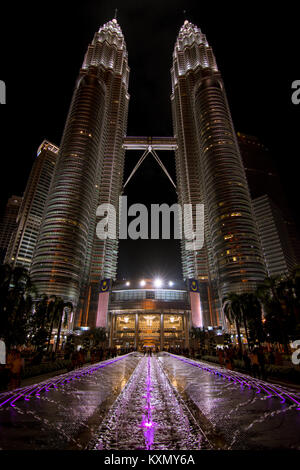 Angolo basso delle Petronas Twin Towers, Kuala Lumpur, Malesia con viola fontana illuminata in primo piano. Foto Stock