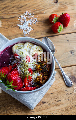 Acai ciotola con cucchiaio e ingredienti - ciotola di acai purea con condimenti di banana, fragola, granola e semi. Foto Stock