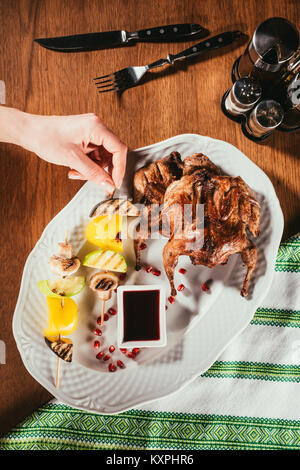 Vista superiore della mano femminile prendendo pezzo di verdure alla griglia dalla piastra con pollo fritto Foto Stock