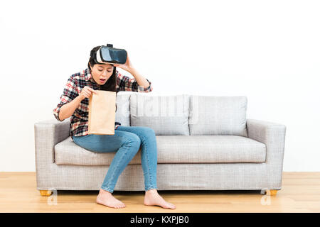 Giovane donna graziosa utilizzando dispositivo VR sperimentando 3D gioco arrivare vertigini e seduto sul pavimento in legno divano divano vomito in sfondo bianco. Foto Stock