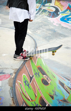 Raccolto di tredici anni di bilanciamento del maschio il suo skateboard sul bordo di un pendio a skate park coperto di graffiti Foto Stock