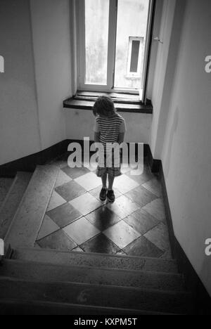 Un bambino di otto anni si erge su una rampa di scale che guarda il pavimento piastrellato Foto Stock