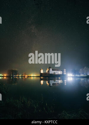 Vista panoramica del complesso del Castello di Mir nella notte con cielo stellato e candelette di riflessione sul lago. Punto di riferimento in Bielorussia Foto Stock